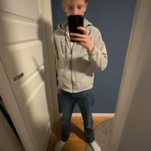 Grå hoodie från Sail Racing med dragkedja - Säljer en grå hoodie från Sail Racing med hel dragkedja framtill och huva. Tröjan har långa ärmar och två fickor på sidorna. Perfekt för dig som gillar en enkel och stilren look. Passar till jeans eller joggers.