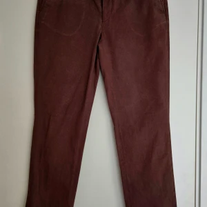 Bruna byxor från Filippa K i bomull - Bruna byxor från Filippa K i rak modell. Bomull, med klassisk passform och fickor framtill. Varm brun ton. Fållen har delvis gått upp på ena byxbenen. 