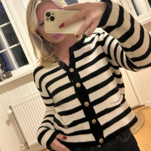 Randig kofta med guldknappar - Snygg stickad kofta i svart och vitt med breda ränder och dekorativa guldknappar framtill. Koftan har två små fickor och en klassisk rund halsringning. Perfekt att slänga på sig för en trendig look. Storlek S🌸🌸💖💖