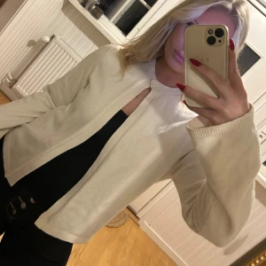 Vit kofta med knapp i halsen - Säljer en stilren vit kofta med lång ärm och rund halsringning. Koftan har en enkel knapp högst upp vid halsen och är öppen framtill. Materialet känns mjukt och är ribbstickat vid kanterna. Perfekt att slänga över en topp för en clean look. Storlek M men passar en S också💖💖🌸🌸