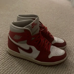 Nike Air Jordan 1 High röd/vit - Säljer ett par klassiska Nike Air Jordan 1 High i rött och vitt skinn. Skorna har ikoniska Air Jordan-loggan på sidan, röda snören och vit sula. Perfekt för dig som vill sticka ut med en tidlös sneaker med högt skaft och snygg design.
