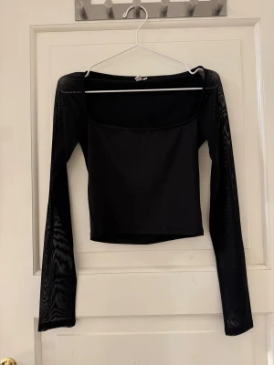 Svart mesh topp från Nelly, S - Svart långärmad topp från Nelly i storlek S. Toppen har mesh-ärmar och en fyrkantig urringning som ger en snygg och modern look. Materialet är polyester och elastan, vilket gör den stretchig och bekväm. Använd två gånger. 