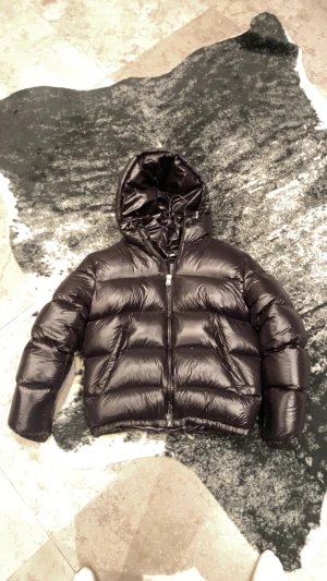 Zara puffer - Säljer en svart pufferjacka från Zara i storlek M. Jackan har en glansig finish, huva och dragkedja framtill. Den är vadderad och har en boxig, lite oversized passform som ger en cool look. Perfekt för kalla dagar när du vill hålla stilen.