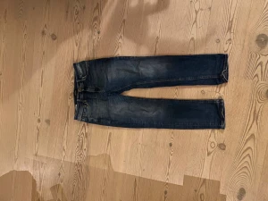 Jack & Jones Regular Clark jeans blå - Snygga blå jeans från Jack & Jones, modell Regular Clark. Klassisk femficksdesign med raka ben och normal passform. Jeansen har slitningar och kontrastsömmar, tillverkade i robust denim med detaljer i metall. Perfekt för dig som gillar en enkel och stilren look.