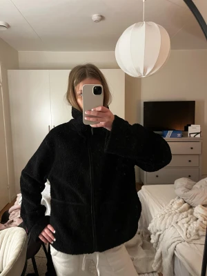 Svart teddyjacka i storlek M - Mysig svart teddyjacka med dragkedja och hög krage. Jackan har en loose passform och är perfekt för kyligare dagar. Tillverkad i mjukt fleece-material som ger en skön och avslappnad vibe.