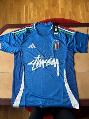 Italien x Adidas x Stüssy edition strl. M - Blå Italien fotbollströja från Adidas i samarbete med Stüssy. Storlek M. Passar både på fotbollsplanen eller som vardaglig stil om man gillar street look. Sitter bra på kroppen