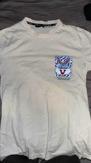 Off-White x Bugs Bunny t-shirt vit/beage M - Vit t-shirt från Off-White i samarbete med Warner Bros, med stor Bugs Bunny-grafik och blå/vita detaljer både fram och bak. Klassisk passform och rund hals. Perfekt för dig som gillar streetwear och unika prints.