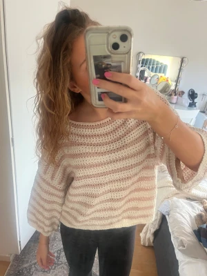 Randig stickad tröja  - Supermysig stickad tröja med breda, ljusrosa och vita ränder. Tröjan har en loose passform, trekvartsärmar och är croppad i modellen. Perfekt för dig som gillar en chill och avslappnad stil. Snygg att bära offshoulder för en extra cool vibe.