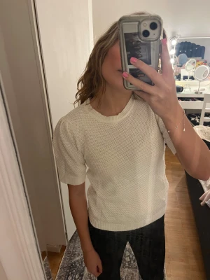 Vit stickad kortärmad tröja - Säljer en vit stickad tröja med korta ärmar och rund hals. Tröjan har en snygg struktur i materialet och ribbade kanter vid hals och ärmslut. Perfekt för dig som gillar en clean och fräsch look.