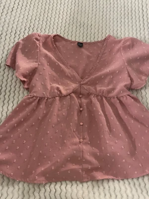 Rosa blus med knappar från SHEIN - Gullig rosa top från SHEIN i storlek XS. Toppen har v-ringning, korta volangärmar och knappar framtill.