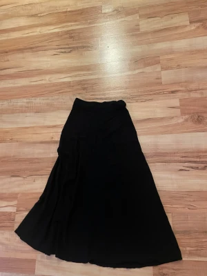 Svart långkjol från NA-KD - En svart långkjol från NA-KD i klassisk A-linjeform. Kjolen har en enkel och stilren design med lätt vidd nertill.