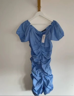 Blå ruched kortklänning Gina Tricot - Supersöt ljusblå kortklänning från Gina Tricot med puffärmar och snygg rynkad effekt framtill. Klänningen har v-ringning och dragkedja i ryggen. Perfekt för dig som vill sticka ut med en trendig och feminin look.