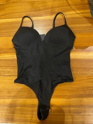 Svart body från H&M, storlek M - Snygg svart body från H&M i storlek M med vadderade kupor och smala axelband. Materialet är mjukt och stretchigt med 94% polyamid och 6% elastan, vilket gör den bekväm och följsam. 