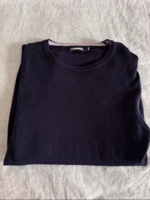 Mörkblå stickad tröja J.Lindeberg - Snygg mörkblå stickad tröja från J.Lindeberg i storlek L. Tröjan har rund hals, långa ärmar och diskret logga på bröstet. Perfekt för dig som gillar stilrena och klassiska plagg med skön passform.