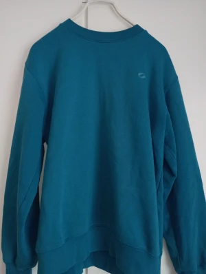 Blå sweatshirt från SOC i XS - En enkel och snygg blå sweatshirt från SOC i storlek XS. Tröjan har rund hals, långa ärmar och en liten logga på bröstet. Mjuk och skön bomullskvalitet som passar perfekt när du vill vara chill. Klassisk passform och ribbade muddar vid ärmslut och nederkant.