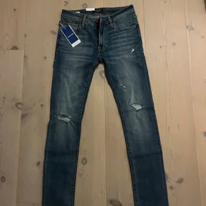 Blå skinny jeans från Jack & Jones - Snygga blå jeans från Jack & Jones med slim fit passform och slitna detaljer på benen. Klassisk femficksmodell med läderpatch bak i midjan. Jeansen har normal midja och är tillverkade i stretchigt denim för skön komfort.