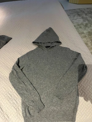 Grå hoodie från Oscar Jacobson XS - Snygg grå hoodie från Oscar Jacobson i storlek XS, men sitter som S tillverkad i Italien. Tröjan är stickad och har en klassisk huva samt långa ärmar med ribbade muddar. Perfekt för dig som gillar stilrena och bekväma plagg med premiumkänsla. litet hål i under armen som man knappt märker.