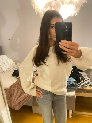 Vit stickad tröja med ballongärmar - Supermysig vit stickad tröja med ballongärmar och rund hals. Tröjan har en loose passform och breda muddar vid ärmslut och nederkant. Perfekt att slänga på sig när det är lite kyligt ute. Passar dig som gillar enkel och stilren look.