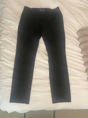 Svarta kostymbyxor från Morris Motala - Svarta golfbyxor från travis matheo i klassisk rak modell. Byxorna har diskreta fickor bak och är tillverkade i ett mjukt bomullsmaterial med lite stretch för extra komfort. Perfekt passform och stilren look för dig som gillar minimalistiskt.