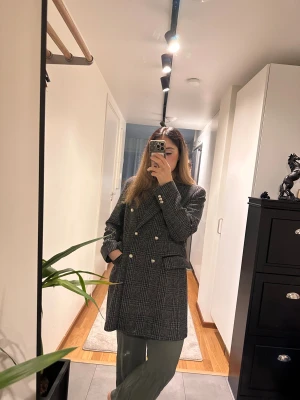 Rutig kappa från MNG med guldknappar - Säljer en snygg rutig kappa från MNG i svart och grått. Dubbelknäppt modell med dekorativa guldknappar och klassisk krage. Kappan har två fickor framtill och är fodrad. Perfekt för dig som gillar en stilren och trendig look.