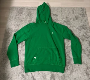 Grön hoodie från Polo Ralph Lauren - Snygg grön hoodie från Polo Ralph Lauren med klassisk logga på bröstet. Tröjan har huva med snörning, stor magficka och långa ärmar. Perfekt för chill dagar och enkel att matcha med jeans eller joggers.