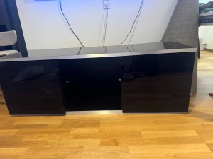 TV-bord / mediabänk i modern svart glasfinish - Säljer ett tv-bord i stilren design med två förvaringsdelar bakom dörrarna. Möblerna är i fint skick och fungerar utmärkt för TV, spelkonsoler eller annan elektronisk utrustning.  Mått: 	•	Längd: 150 cm 	•	Bredd: 50 cm 	•	Höjd: 53 cm (bekräfta gärna om det ska vara 153 cm)  Bordet kan endast hämtas från lägenheten, vi erbjuder ingen leverans. Kontakta oss för att boka avhämtningstid eller om du har ytterligare frågor.