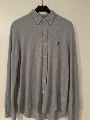 Grå skjorta från Ralph Lauren  - Snygg grå skjorta från Ralph Lauren i featherweight mesh. Klassisk krage, långa ärmar och knappar hela vägen. Diskret broderad logga på bröstet. 