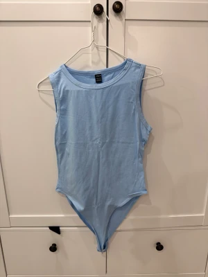 Ljusblå ärmlös bodysuit från SHEIN - Säljer en ljusblå ärmlös bodysuit från SHEIN i storlek L. Enkel och clean design med rund halsringning och mjukt bomullsmaterial. Perfekt att styla med jeans eller kjol för en fräsch look.
