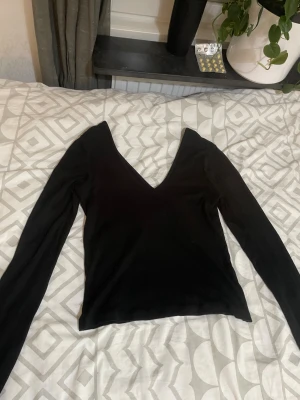 Svart ribbad långärmad topp från Bik Bok - Svart långärmad topp från Bik Bok i storlek M. Toppen har en djup v-ringning och är ribbad i materialet vilket ger en snygg struktur. Öppen rygg samma som i fram.  Passformen är normal och toppen är enkel att matcha med olika stilar.