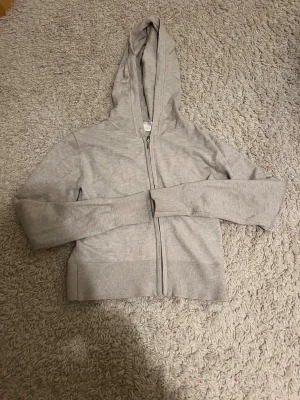  hoodie med dragkedja - Snygg grå hoodie med dragkedja och huva. Tröjan har långa ärmar och breda ribbade muddar vid ärmslut och nederkant. 