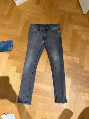 Nudie Jeans - Snygga grå jeans från Nudie Jeans med skinny passform och klassisk femficksdesign. Jeansen har svarta sömmar på bakfickorna och subtilt tvättad look. Perfekt för dig som gillar en smal siluett och stilren vibe. Moddelen heter lean dean 