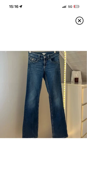 Blå bootcut jeans Gina Tricot 164 - Snygga blå jeans från Gina Tricot i storlek 164. Modellen har bootcut-ben, klassiska fickor med lock och knapp bak samt markerade sömmar. Jeansen är i denim med en cool tvätt och passar perfekt till en trendig vardagslook.