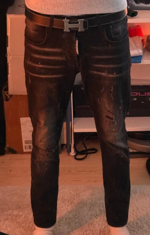 Svarta Dsquared2 jeans med slitningar - Svarta jeans från Dsquared2 i storlek 48. Snyggt slitna detaljer på benen, diskreta färgstänk och en cool tvättad look. Klassisk femficksmodell med Dsquared2-logga på gylfen och orange patch bak.✅✅