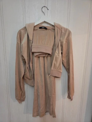 Beige velourset från bikbok - Säljer ett beiget mjukisset från bikbok i velour med breda ben och normal passform. Byxorna har resår i midjan och vida ben i stl S och ziptröjan är i stl XS. Nypris är 300kr/del (600kr/set) säljes för 300kr