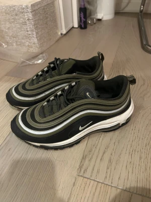 Nike Air Max 97 - Nike Air Max 97 sneakers i olivgrönt, svart och vitt. Skorna har snörning, mesh och syntetmaterial, samt rund tå och platt sula. Använda men i väldigt bra skick