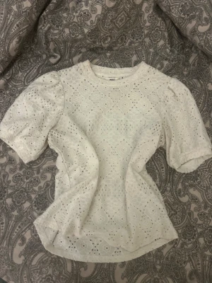 Vit spetsblus från Object - Säljer en vit blus från Object med puffiga korta ärmar och rund hals. Blusen har ett detaljerat spetsmönster med broderade former och små hål, liten smink fläck som går bort i tvätten, tvättar innan jag skickar 💗