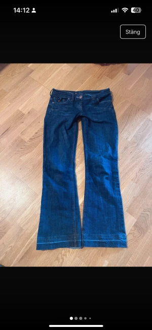 Lågmidjade vintage bootcut jeans med broderi - Snygga lågmidjade mörkblå jeans från Replay med bootcut passform och låg midja. Jeansen har coola broderade detaljer på bakfickan och kontrastsömmar. Klassisk femficksmodell med knapp och dragkedja framtill. Perfekt för dig som gillar unik stil.