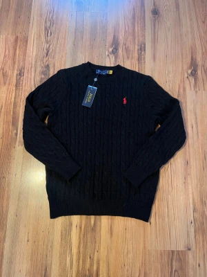 Svart kabelstickad tröja Polo Ralph Lauren - Svart kabelstickad polo Ralph lauren 🐎            Size M/175, måtten - längd (64cm), bredd (46cm), ärmlängd (58cm).                                     10/10 skick, kommer med tag, inga defekter Hör av er om ni har frågor 🤩