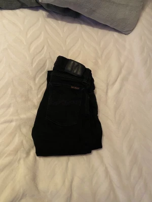 Svarta skinny jeans från Nudie Jeans - Säljer ett par svarta skinny jeans från Nudie Jeans i storlek W27 L32. De har klassisk femficksdesign, smal passform och är tillverkade i mjukt jeansmaterial. Perfekta om du gillar en tajt siluett och stilren look. Skulle säga att de sitter mer som L30.