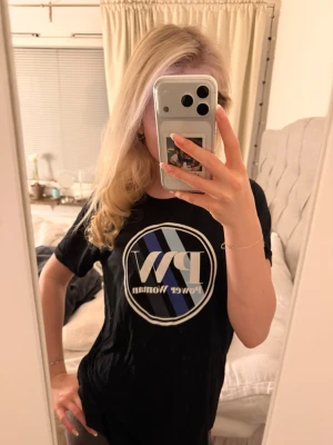 Svart Power Woman t-shirt PW - Snygg svart t-shirt från Pernilla Wahlgren med stort PW Power Woman-tryck i vitt, blått och svart på bröstet. Klassisk rund hals och korta ärmar. Tillverkad i mjuk bomull som känns skön mot huden. Perfekt för dig som vill ha en statement-tee i garderoben.