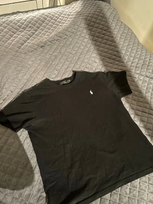 Svart t-shirt från Polo Ralph Lauren - Klassisk svart t-shirt från Polo Ralph Lauren med den ikoniska broderade loggan på bröstet. T-shirten har rund halsringning och korta ärmar. Tillverkad i mjuk bomull som är skön att bära hela dagen.