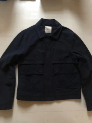 Mörkblå overshirt från mango herr  - Stilren mörkblå overshirt från Mango med klassisk krage och stora fickor framtill. Tillverkad i bomull och har knappar längs hela framsidan. Perfekt att bära som lager över en t-shirt eller skjorta för en avslappnad men snygg look.