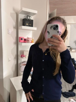 Mörkblå klassisk kofta med knappar - En stilren mörkblå kofta med knäppning framtill och långa ärmar. Koftan har en enkel och tidlös design som passar perfekt till både jeans och kjol. Materialet ser mjukt och bekvämt ut, perfekt för lager-på-lager-stil.