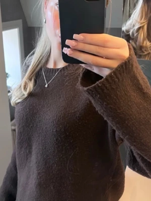 Brun stickad tröja med rund hals - Mysig brun stickad tröja med rund hals och långa ärmar. Tröjan har en enkel och avslappnad passform, perfekt för lager-på-lager och chill dagar. Materialet ser ut att vara mjukt och fluffigt, vilket ger en skön känsla.