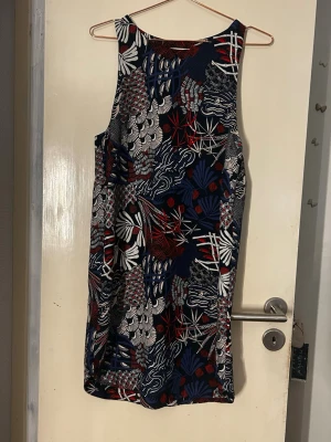 Mönstrad ärmlös kortklänning - Säljer en cool ärmlös kortklänning med färgstarkt mönster i marinblått, vitt och rött. Klänningen har en rak passform och är perfekt för dig som gillar statement-plagg. Materialet känns lätt och passar bra till varmare dagar.