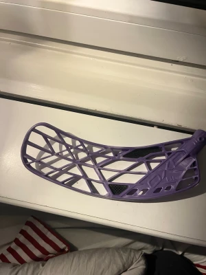 Lila innebandyblad OXDOG FSL - Säljer ett lila innebandyblad från OXDOG med ett öppet, lättviktigt mönster och svarta detaljer. Bladet är tillverkat i plast och har en modern design som passar perfekt för dig som vill ha bra bollkontroll och skott.