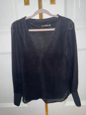 Svart v-ringad blus från Mango - Stilren svart blus från Mango med v-ringning och långa ärmar. Tillverkad i ett tunt, lätt material som ger en luftig känsla. Perfekt att matcha med jeans eller kjol för en trendig look.