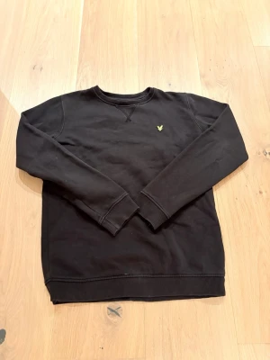 Svart sweatshirt från Lyle & Scott - Klassisk svart sweatshirt från Lyle & Scott med rund halsringning och det ikoniska gula örnlogot på bröstet. Tröjan har ribbade muddar vid ärmslut och nederkant samt en relaxed passform. Perfekt basplagg för en stilren och enkel look.                         Tveka inte för att hör av dig vid minsta fundering😊
