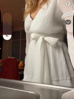 Studentklänning  - Superfin vit kort omlottklänning från Dennis Maglic med långa ärmar och volangdetaljer. Klänningen har knyt i midjan och är gjord i ett glittrigt, lätt material som ger en lyxig känsla. Perfekt för sommarens alla tillfällen som exempelvis student 💕! (aldrig använd av mig, men köpt på vinted) Obs någon liten missfärgning vid v-ringning, men inget som syns när man har klänningen på! 