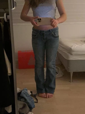 Blå bootcut jeans ifrån miss me - Säljer ett par blå bootcut jeans ifrån miss me med vita kontrastsömmar och dekorativa fickor bak. Jag har köpt dom för 850 spänn i en second hand butik. Dom e för stora därför säljer jag. Jeansen har låg midja och detaljerade knappar samt ficklock. Perfekta för dig som gillar en avslappnad men ändå snygg stil.